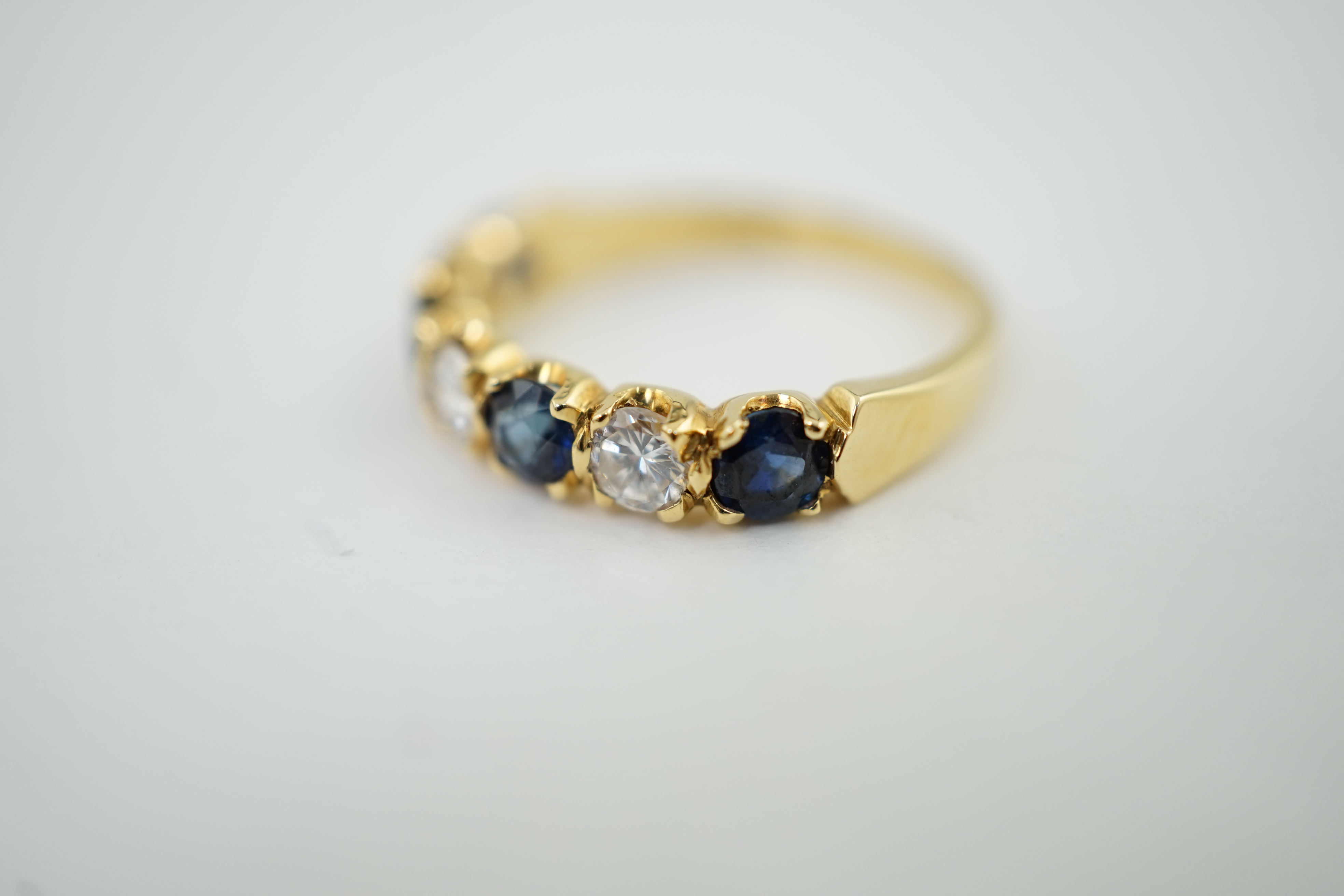 A modern 18ct gold, four stone sapphire and three stone diamond set half hoop ring